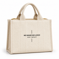 A cream-colored canvas tote bag with gold-tone zipper hardware and black placeholder text reading 'NO NAME NO LOGO JUST IMPACT' on the front, set against a plain white background.